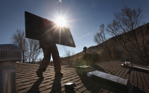 Men install solar panel on roof of house.